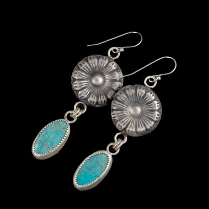 Sterling silver concho dangle earrings with hand-stamped floral detailing and bezel-set oval turquoise stones – Southwestern-inspired artisan jewelry by Divella Designs, shown on black background.