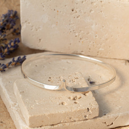 Silver wishbone bracelet on a stone surface with lavender flowers