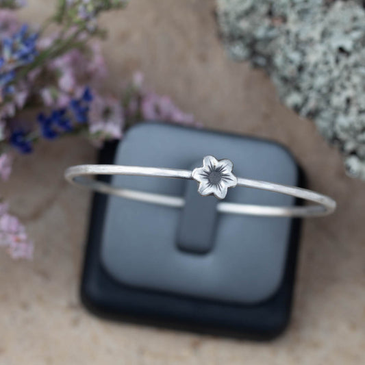 Sterling silver flower bangle bracelet by Divella Designs, handmade in Vermont with smooth satin finish and sculpted blossom on 2 1/2" band, styled with birch bark