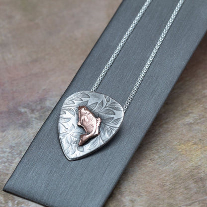 Handcrafted sterling silver pendant with etched floral background and raised copper jumping bass fish, hung on a silver chain – rustic nature-inspired necklace by Divella Designs, displayed on dark backgroun