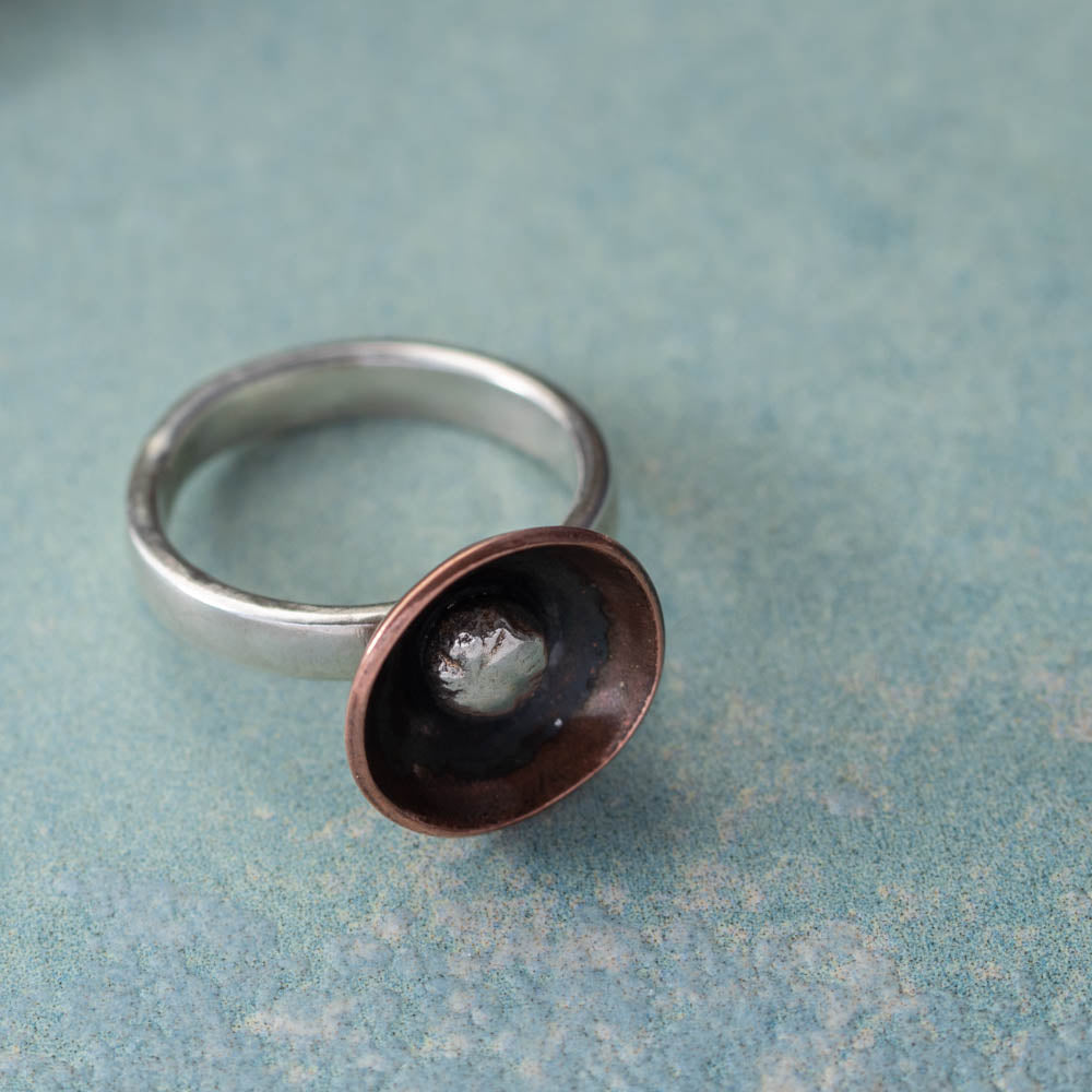 Handmade sterling silver and copper ring with dark patinated interior on a soft blue surface