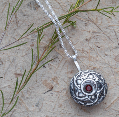 Handcrafted sterling silver pendant necklace featuring a deep red garnet gemstone in a floral shadowbox design, with intricate botanical detailing and oxidized vintage finish