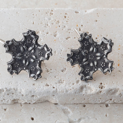 Pair of silver snowflake leaf-shaped earrings on a textured stone surface