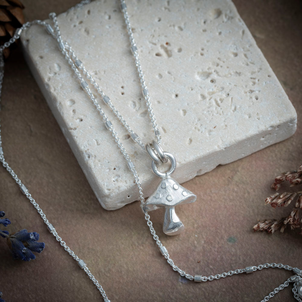 Silver necklace with a mushroom pendant on a textured surface