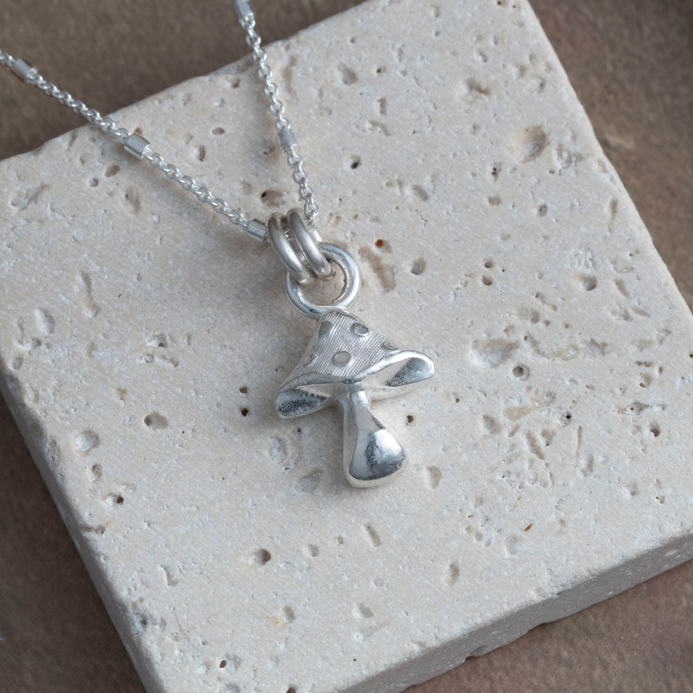 Silver necklace with a unique mushroom pendant on a textured stone surface