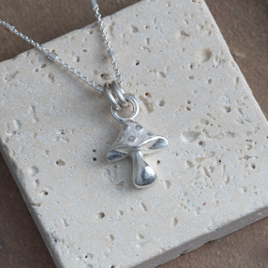 Silver necklace with a unique mushroom pendant on a textured stone surface