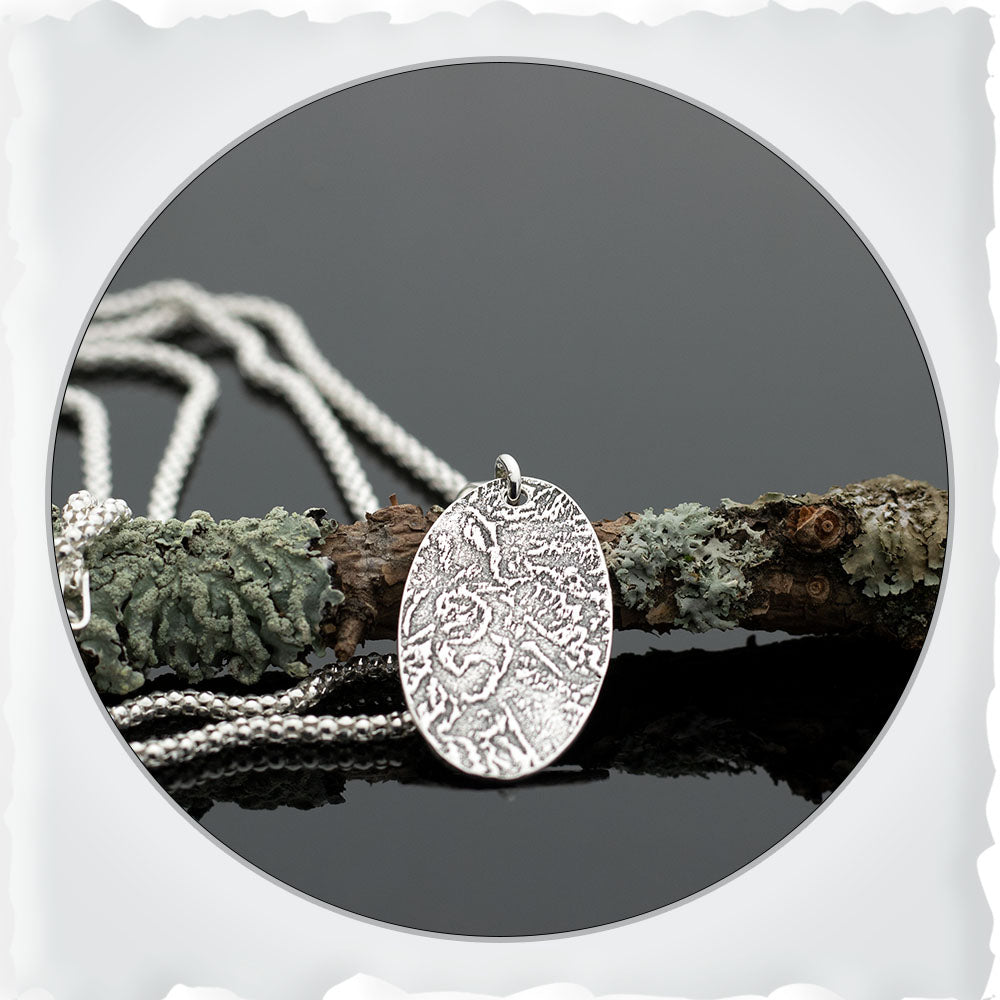 Sterling silver oval pendant necklace with textured landscape design on 18-inch chain.
