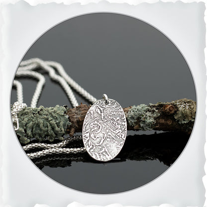 Sterling silver oval pendant necklace with textured landscape design on 18-inch chain.