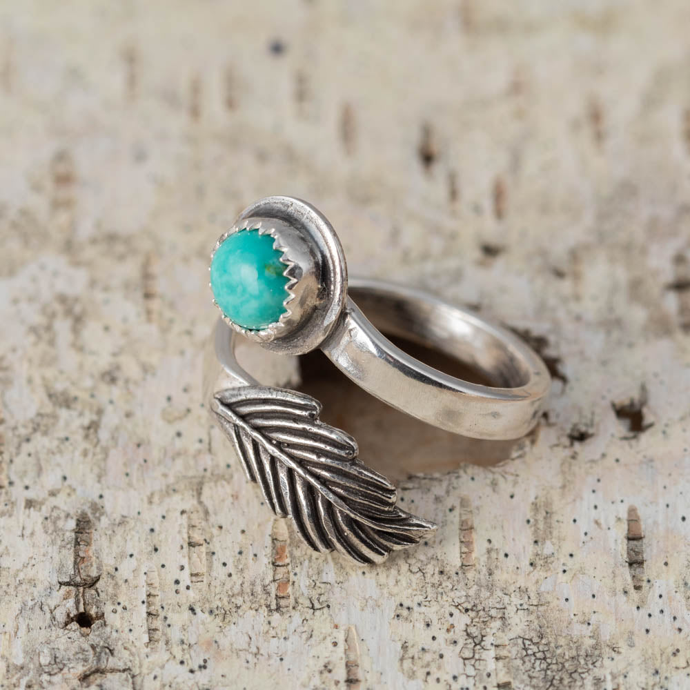 Silver ring with turquoise stone and feather design on a textured surface