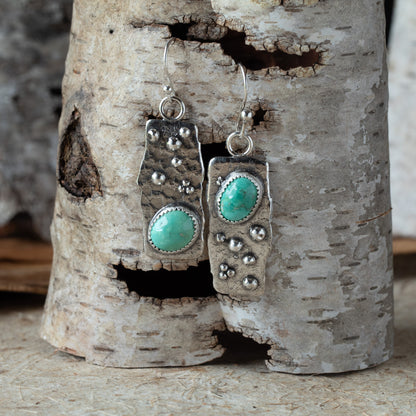 Silver earrings with turquoise stones hanging on a piece of birch wood.
