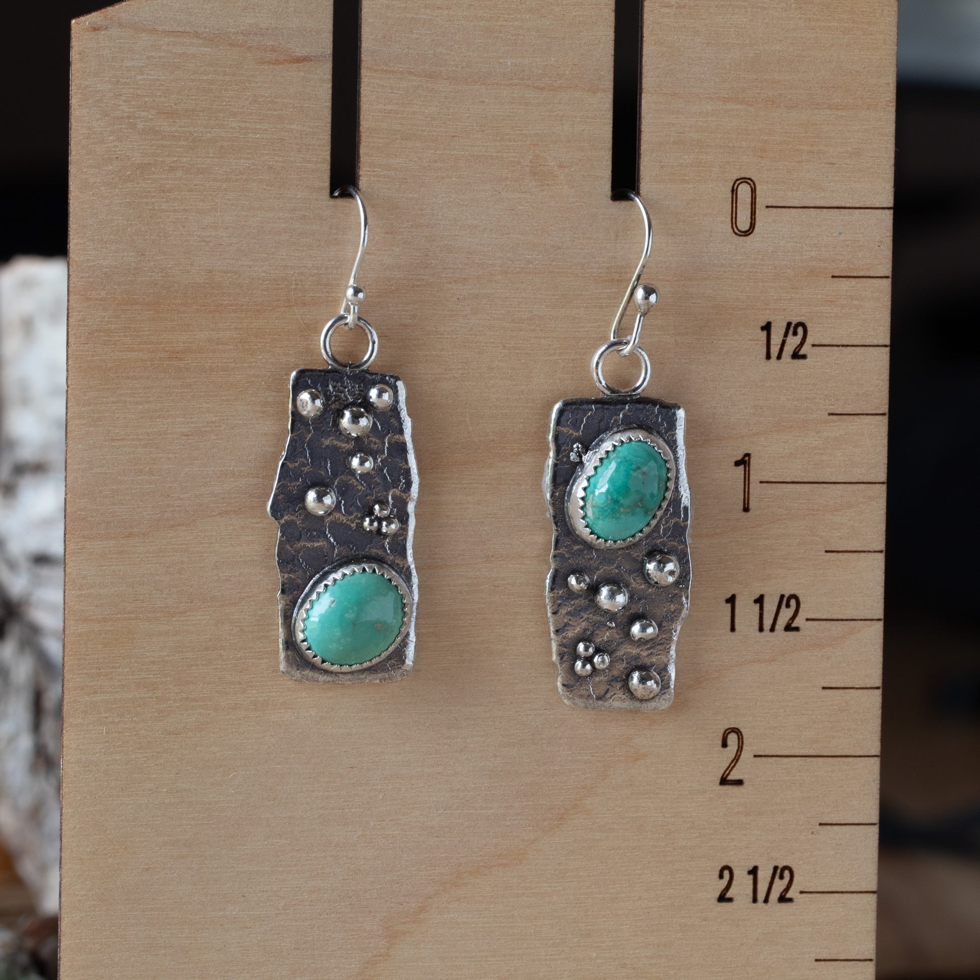 Pair of silver earrings with turquoise stones on a wooden ruler for scale.