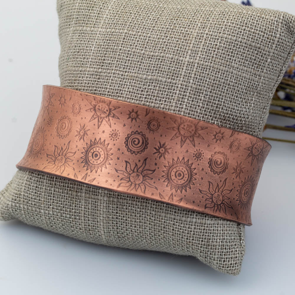 Anticlastic copper cuff bracelet with sun and spiral pattern displayed on linen pillow.