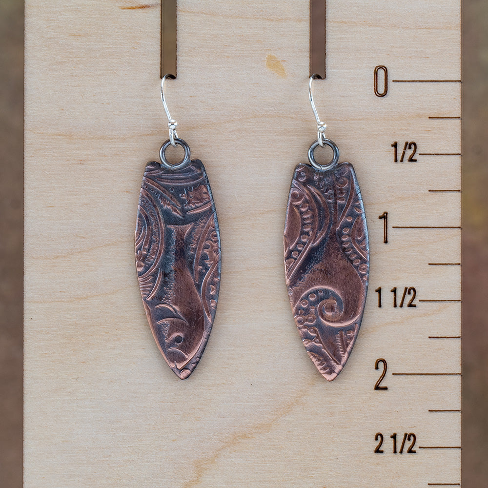 Copper surfboard earrings with impressed swirl texture, oxidized patina, polished highlights, and sterling silver ear wires, handmade by Divella Designs in Vermont.
