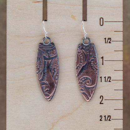 Copper surfboard earrings with impressed swirl texture, oxidized patina, polished highlights, and sterling silver ear wires, handmade by Divella Designs in Vermont.