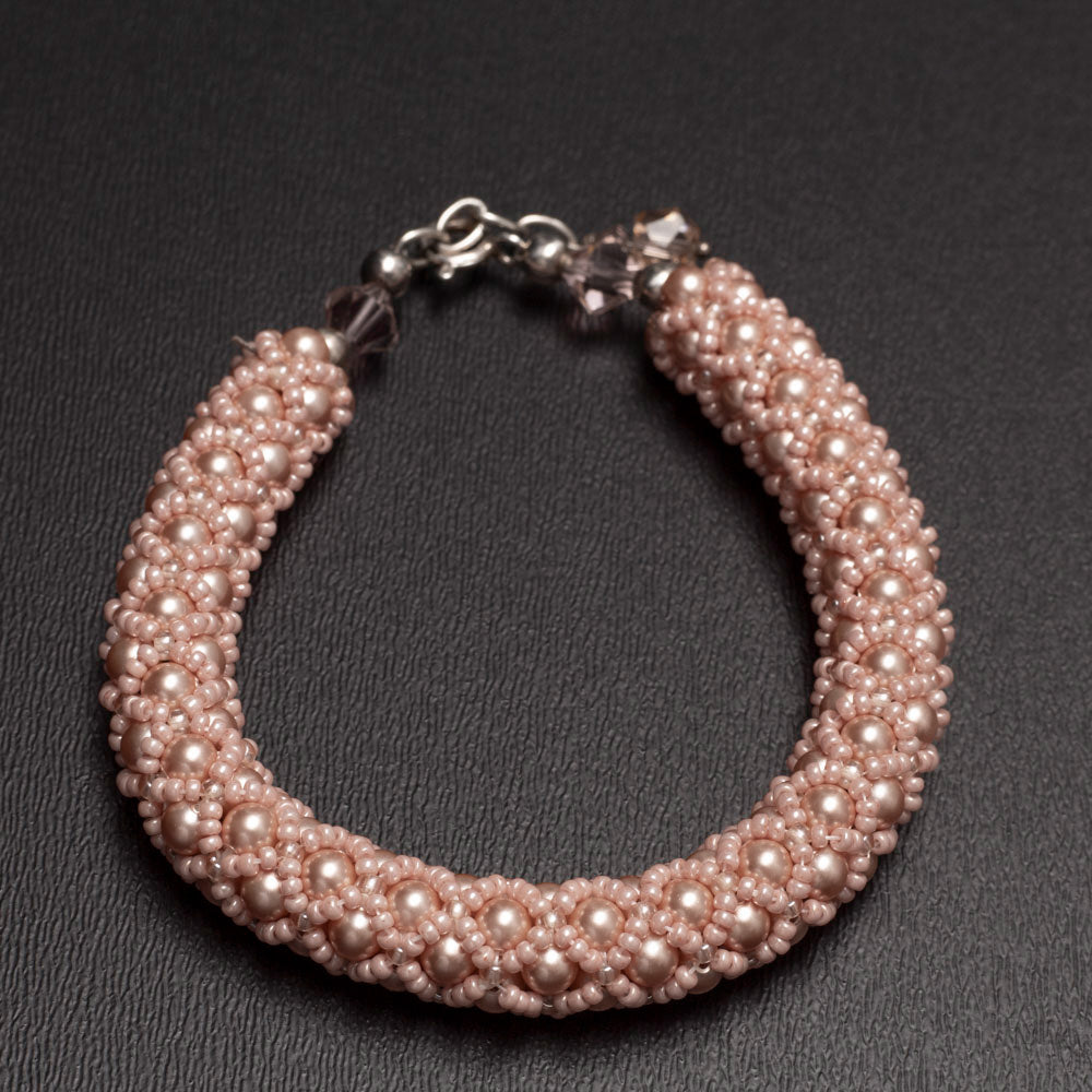 Peach rose beaded bangle bracelet made with Swarovski pearls, displayed on rustic weathered wood with sprigs of greenery in the background.