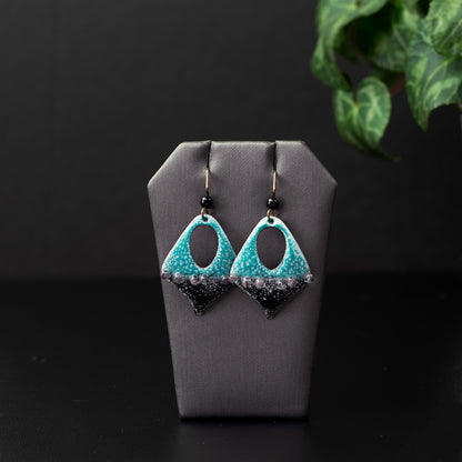 Teardrop cutout enamel earrings in teal and black with raised dot accents, handmade on copper with niobium ear wires and glass bead detail.