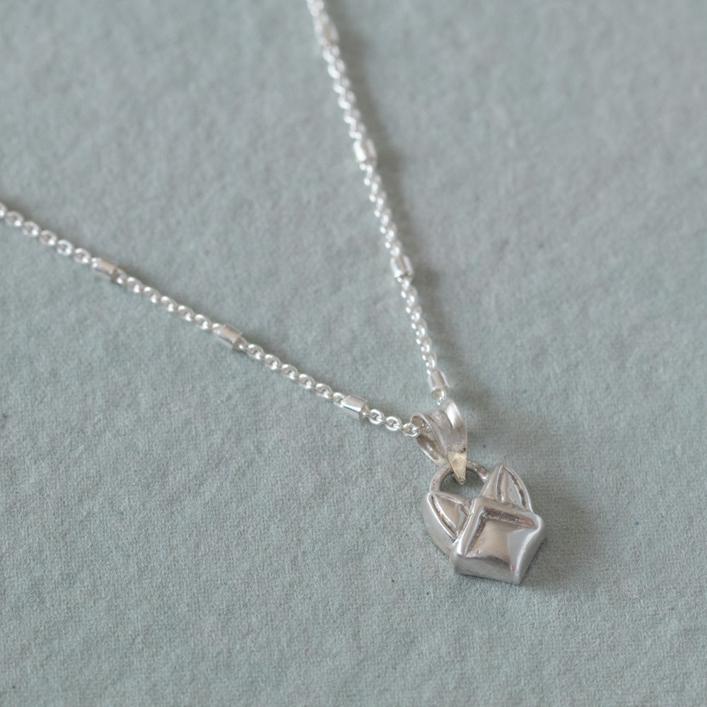 A sterling silver necklace with a small, faceted geometric pendant shaped like a stylized fox head, resting on a textured light gray surface.