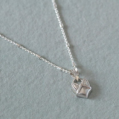 A sterling silver necklace with a small, faceted geometric pendant shaped like a stylized fox head, resting on a textured light gray surface.