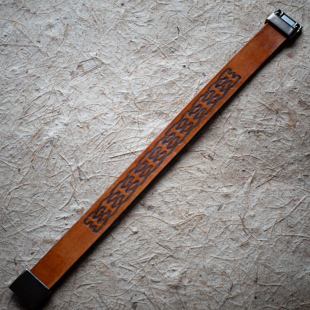 Brown leather strap with dark embossed pattern on a textured beige surface