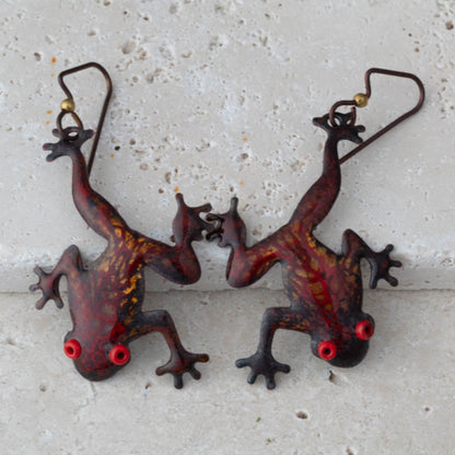 Enameled copper tree frogs in red and gold on a stone surface.