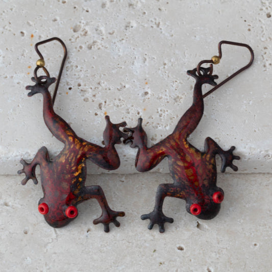 Enameled copper tree frogs in red and gold on a stone surface.