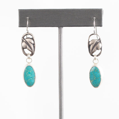 Handcrafted sterling silver drop earrings with sculpted blossom design and oval turquoise gemstones, nature-inspired artisan jewelry by Divella Designs – shown on white background.