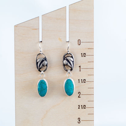 Handcrafted sterling silver drop earrings with sculpted blossom design and oval turquoise gemstones, nature-inspired artisan jewelry by Divella Designs – shown on ruler for scale