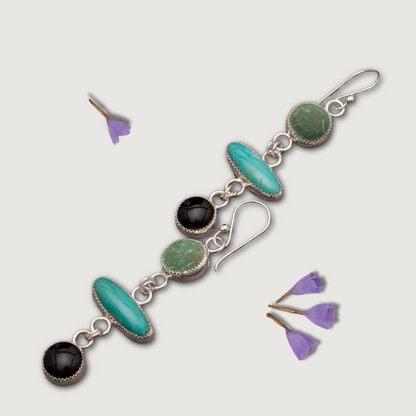 Handmade sterling silver earrings with turquoise, malachite, and onyx gemstones, arranged in a vertical drop design, displayed with small purple flower petals.