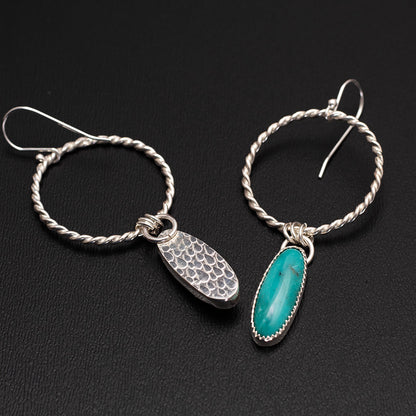 Sterling silver hoop earrings featuring oval turquoise stones on one side and hand-textured silver backs, with front and back of earrings shown on a black background.