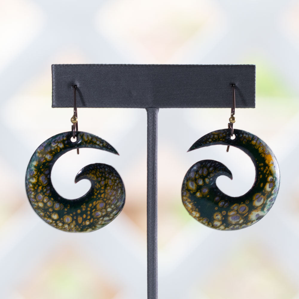 Artisan enamel spiral earrings in rich forest green with golden and violet organic patterning, crafted with niobium ear wires, photographed on a natural stone background.