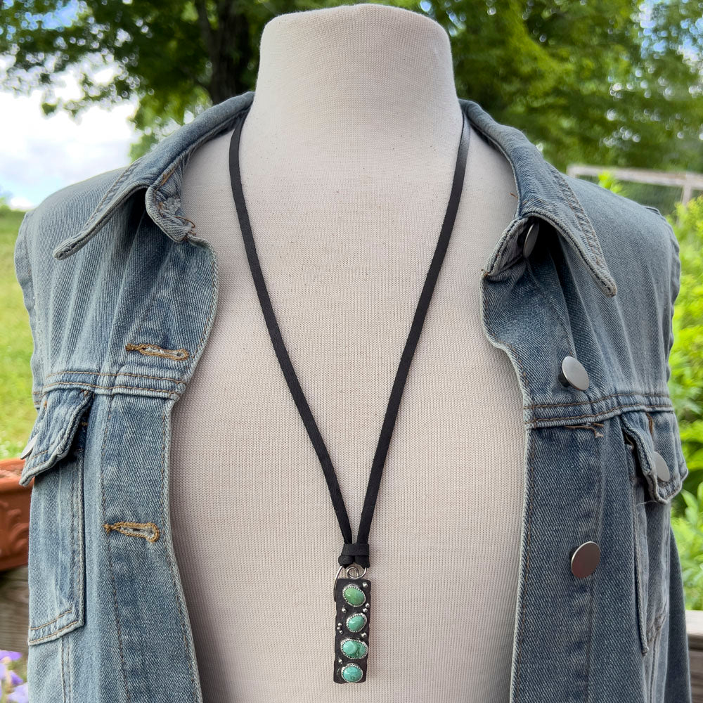 Necklace with a turquoise pendant on a mannequin wearing a denim jacket outdoors.