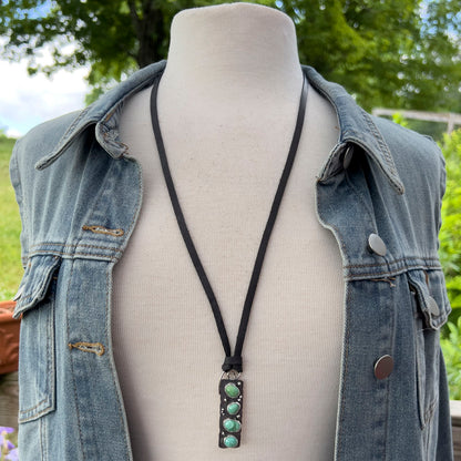 Necklace with a turquoise pendant on a mannequin wearing a denim jacket outdoors.