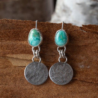 Pair of earrings with turquoise stones and silver discs on a wooden surface