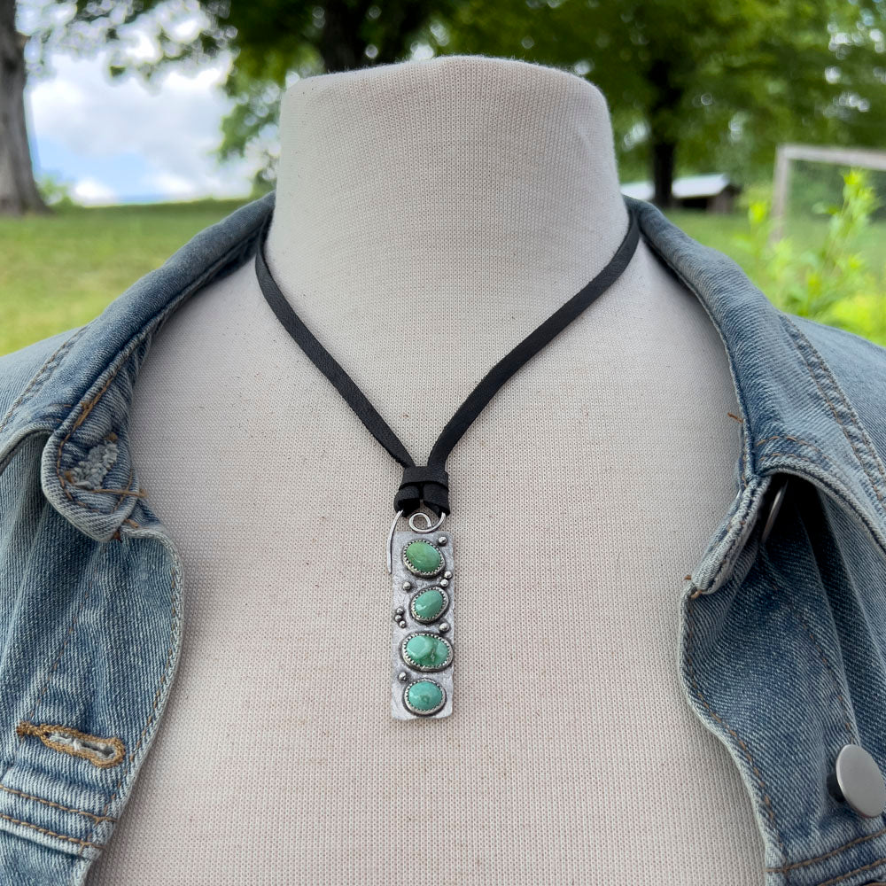 Necklace with a turquoise pendant on a mannequin bust wearing a denim jacket outdoors.