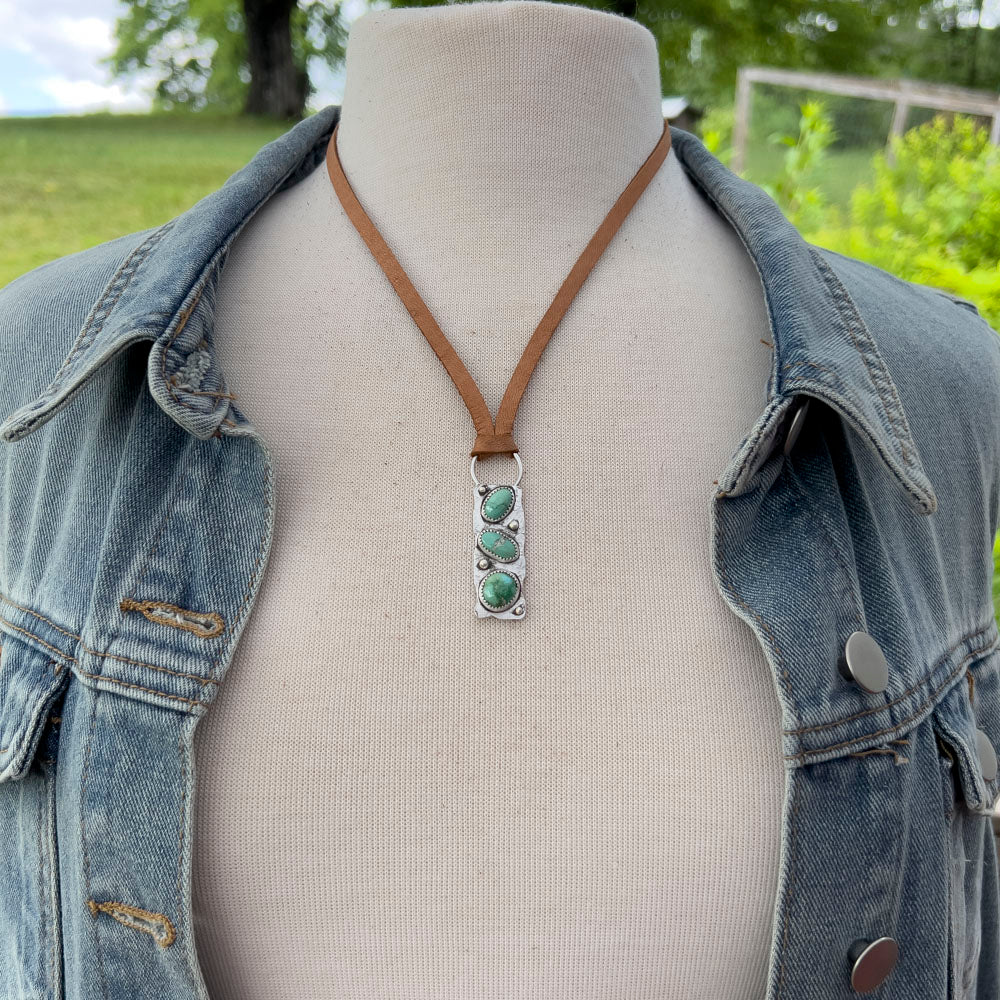 Mannequin wearing a denim jacket with a necklace featuring a Verde Valley pendant outdoors.