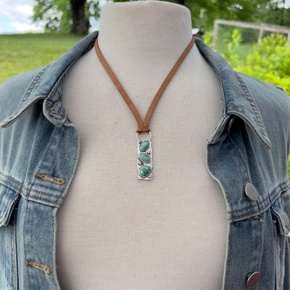 Mannequin wearing a denim jacket with a necklace featuring a Verde Valley pendant outdoors.