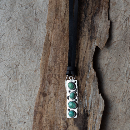 Necklace with a silver pendant featuring three turquoise stones on a textured stone background