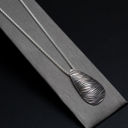 Handmade sterling silver necklace with teardrop pendant featuring a flowing wave texture, modern artisan design on a sterling popcorn chain.