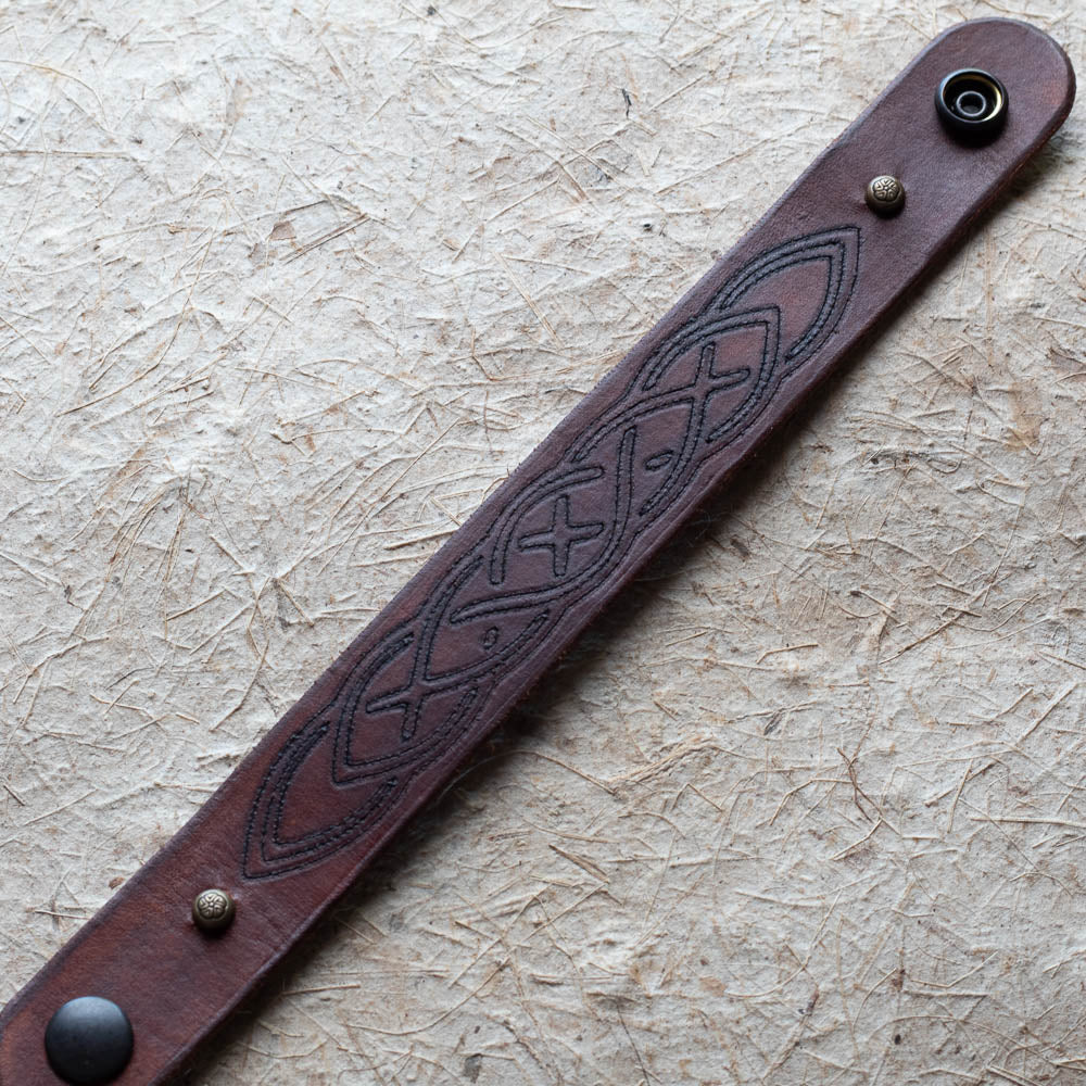 Brown leather bracelet with embossed design on a textured beige surface