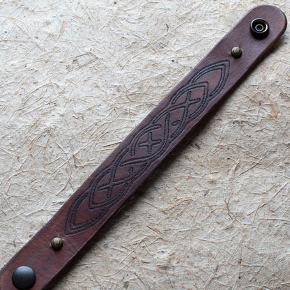 Brown leather bracelet with embossed design on a textured beige surface