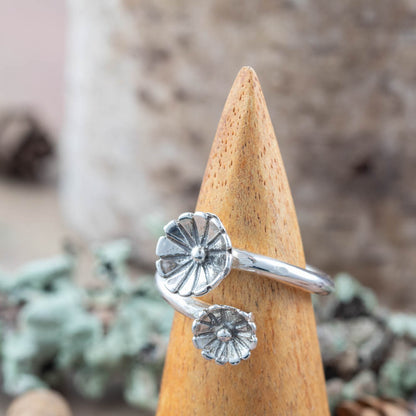 Silver ring with floral design on a wooden cone against a natural background