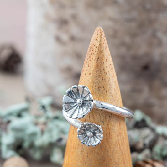Silver ring with floral design on a wooden cone against a natural background