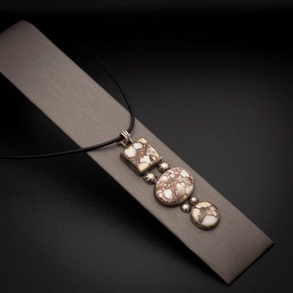 Three-stone Wild Horse pendant with sterling silver accents on a black leather cord, photographed on a neutral display