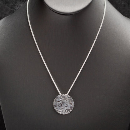 Handmade sterling silver necklace with round pendant featuring etched wild vine botanical design, oxidized finish on a delicate chain.