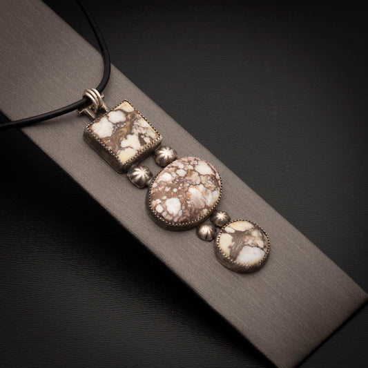 Three-stone Wild Horse pendant with sterling silver accents on a black leather cord, photographed on a neutral display.