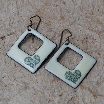 Ivory kiln-fired enamel open square earrings with tiny green wildflower heart design and darkened edges.