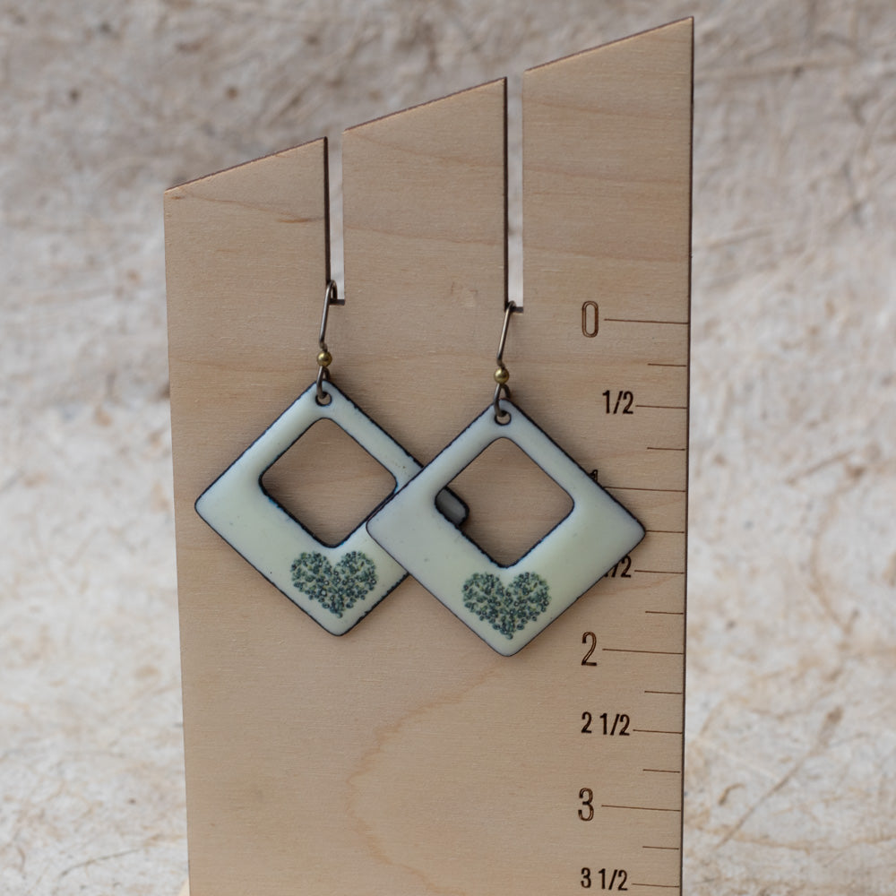 Ivory kiln-fired enamel open square earrings with tiny green wildflower heart design and darkened edges.