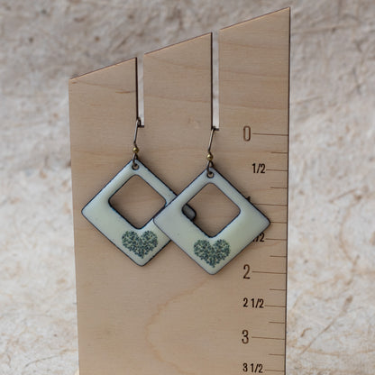 Ivory kiln-fired enamel open square earrings with tiny green wildflower heart design and darkened edges.