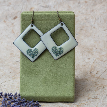 Ivory kiln-fired enamel open square earrings with tiny green wildflower heart design and darkened edges.