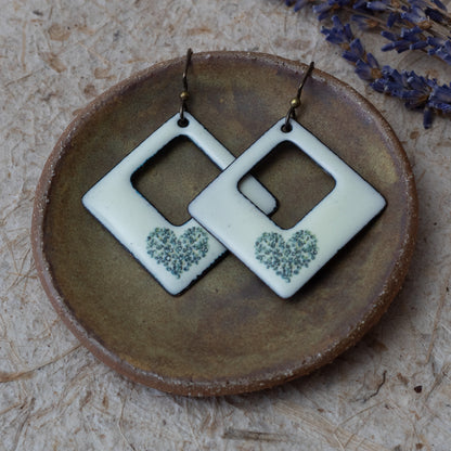 Ivory kiln-fired enamel open square earrings with tiny green wildflower heart design and darkened edges.